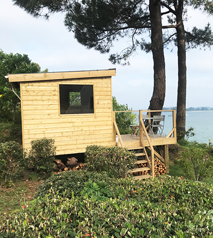 Cabane en bois au bord de l'eau, arbres autour.